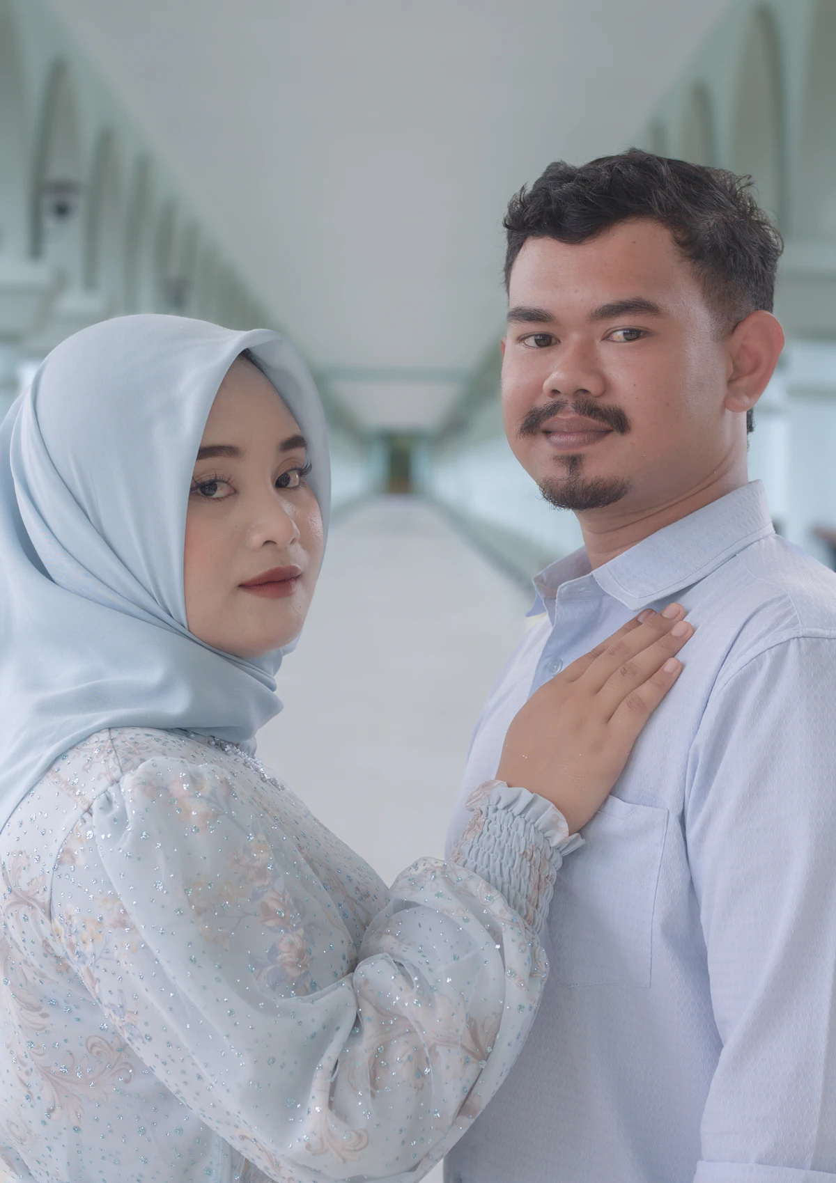 A couple in matching light-blue outfits, the woman wearing a hijab